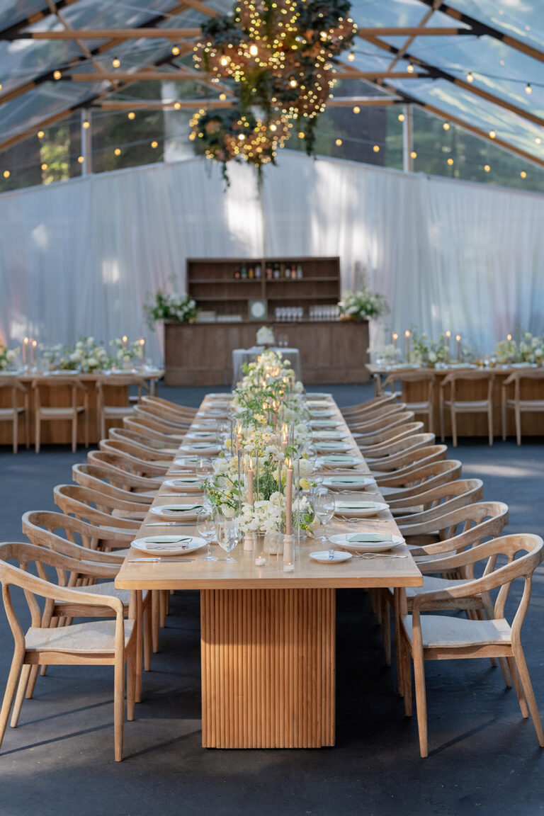 Long banquet table set with candles and greenery under a lit tent at Nestldown